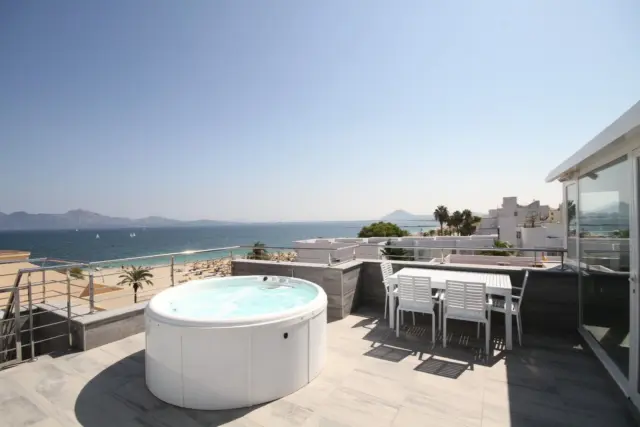 Top-floor apartment available for holiday rental, with private rooftop terrace featuring a jacuzzi and barbecue, plus parking. This first-line beachfront apartment in Puerto Pollensa comprises 2 bedrooms, 2 bathrooms, and a bright open-plan living-dining room with kitchen. It offers sea views from the aluminium windows, porcelain tile flooring, built-in wardrobes, and air conditioning. The apartment is sold fully furnished. Having the sea and beach right outside your door is a luxury enjoyed by this top-floor apartment in Puerto Pollensa. This popular coastal town is known not only for its wide range of water sports and marina, but also for its walking and cycling route along the entire Bay of Pollença. Particularly popular with families, the village is excellently equipped with shops, a health centre, sports facilities, restaurants, and bars. Just steps from the Serra de Tramuntana, Puerto Pollensa is also for hiking enthusiasts. Whether as a primary residence, a profitable second home, or an investment, this top-floor apartment in Puerto Pollensa with holiday rental potential offers many different ways to enjoy this convenient combination. With sea views, a cocktail in hand while relaxing in the jacuzzi on the rooftop terrace, enjoying an impromptu barbecue with friends, or taking a morning walk along the beach: Puerto Pollensa is simply a wonderful place to unwind.
